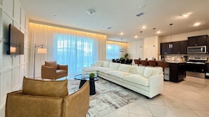Uma sala de estar moderna com sofá, cadeiras, mesa de centro e área de cozinha com armários e eletrodomésticos.