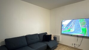 Un salon avec un canapé de couleur sombre, un téléviseur à écran plat fixé au mur et un plancher en bois.