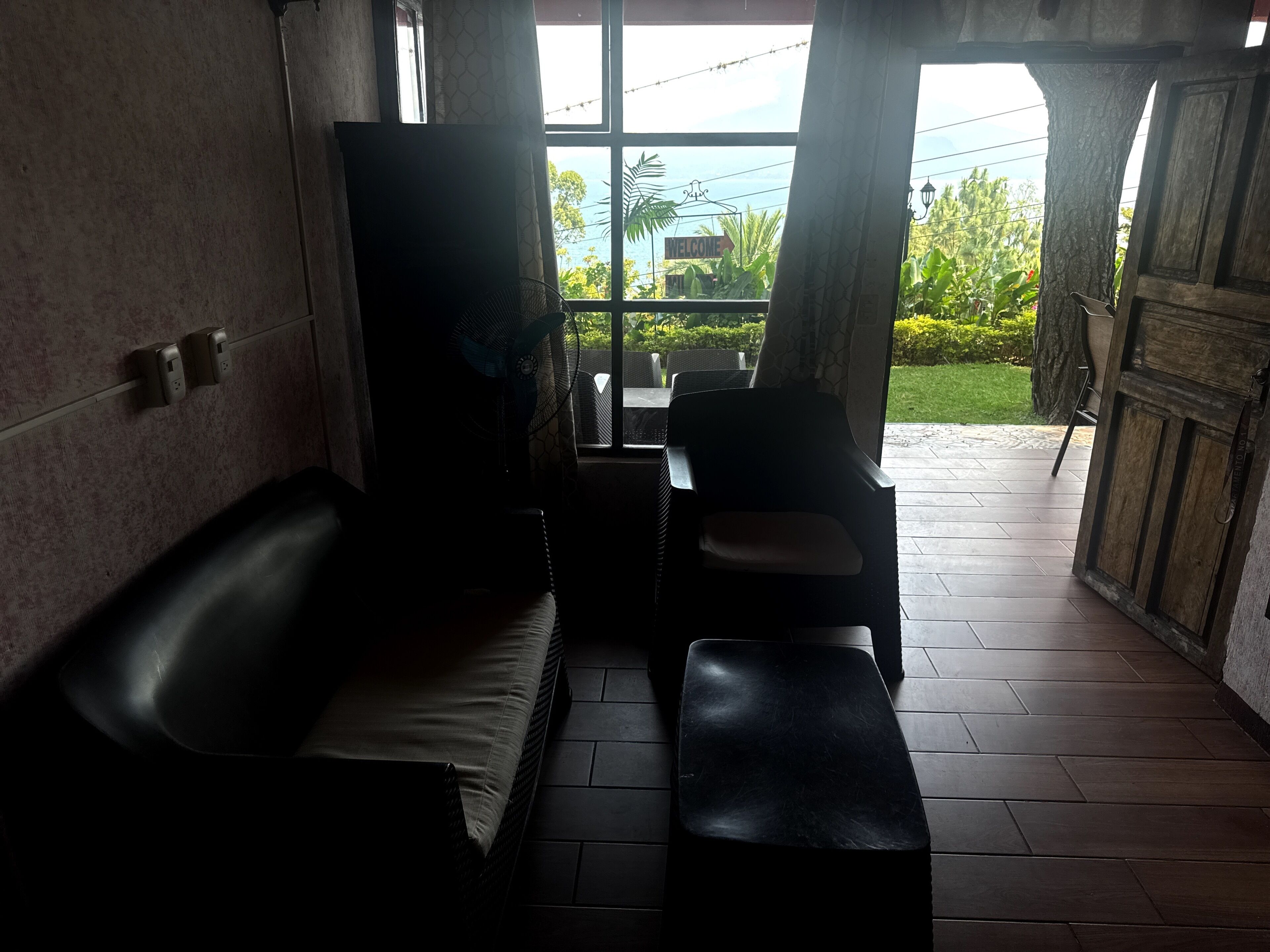 A room with a sofa, a chair, a fan, and a view of the outdoors.