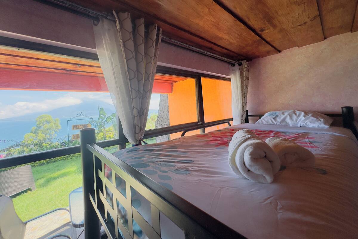 A bedroom with a bed, a view of the outdoors, and a window with curtains.