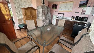 Een eethoek met een glazen tafel en metalen stoelen, een houten kast en een keuken met een fornuis en spoelbak.