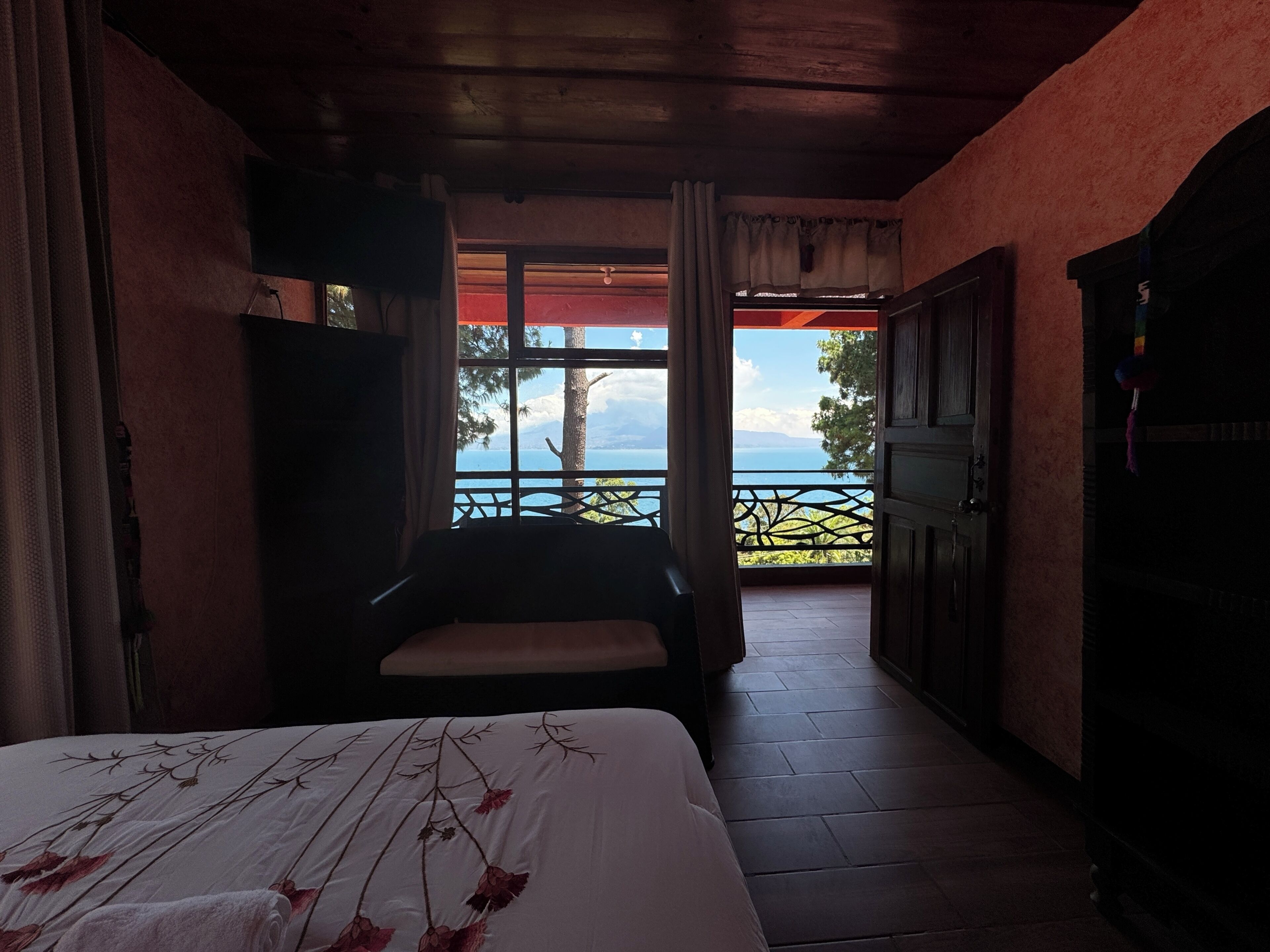 A bedroom with a bed, a chair, a wardrobe, and a view of the outdoors.
