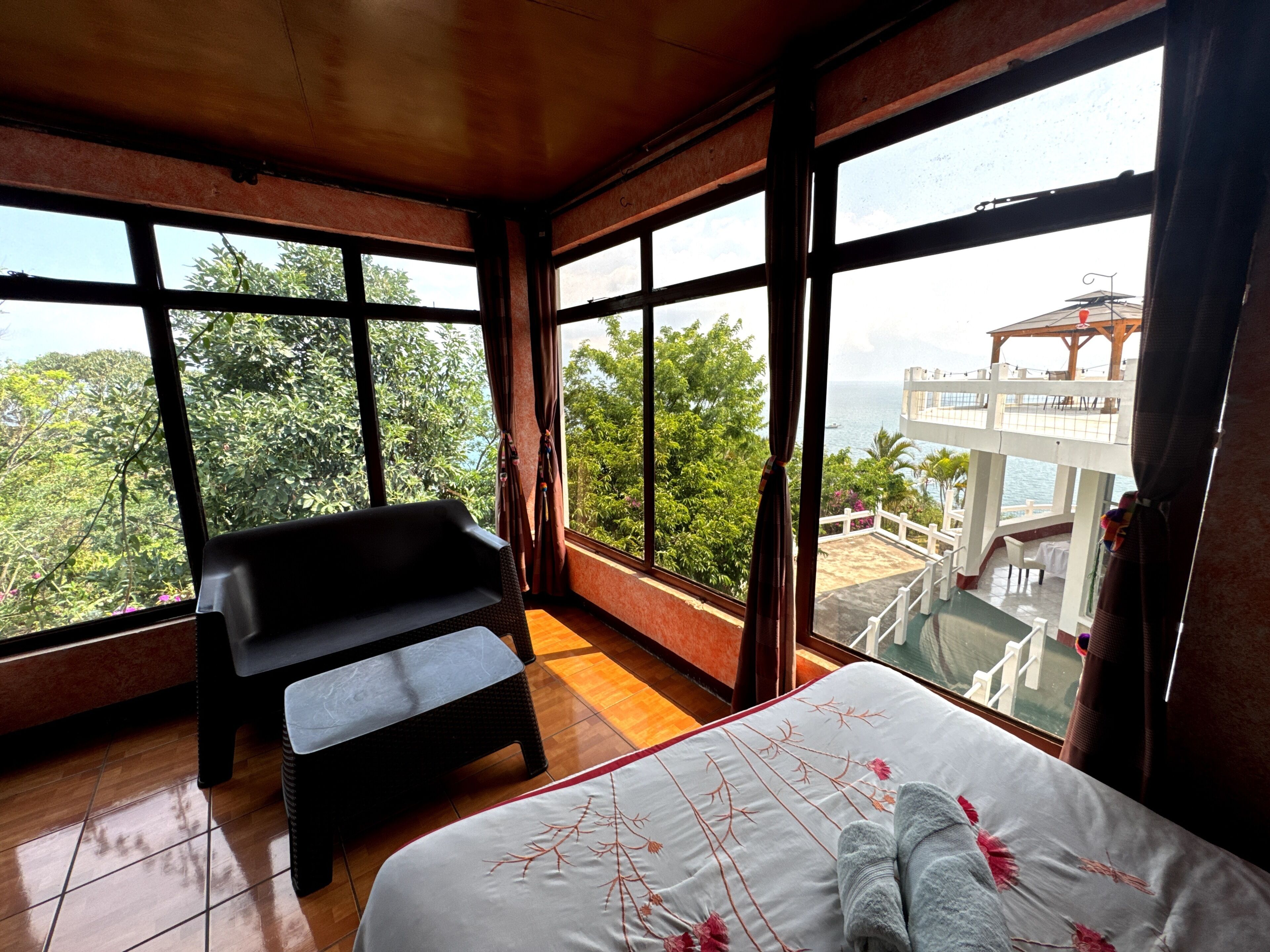 A room with a bed, a bench, and large windows offering a view of greenery and a building.
