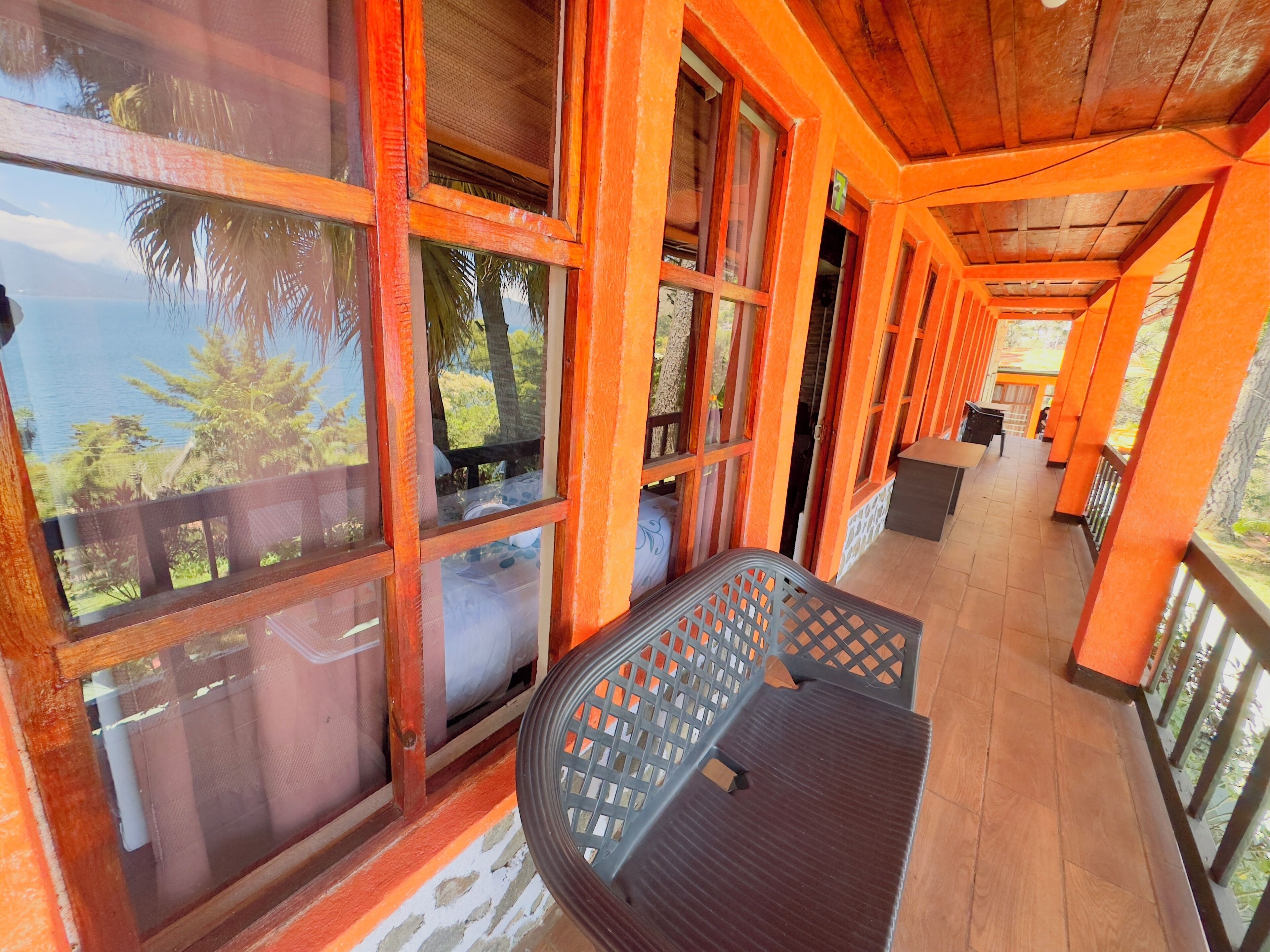 A covered outdoor area with wooden beams and large windows, a table, and chairs.