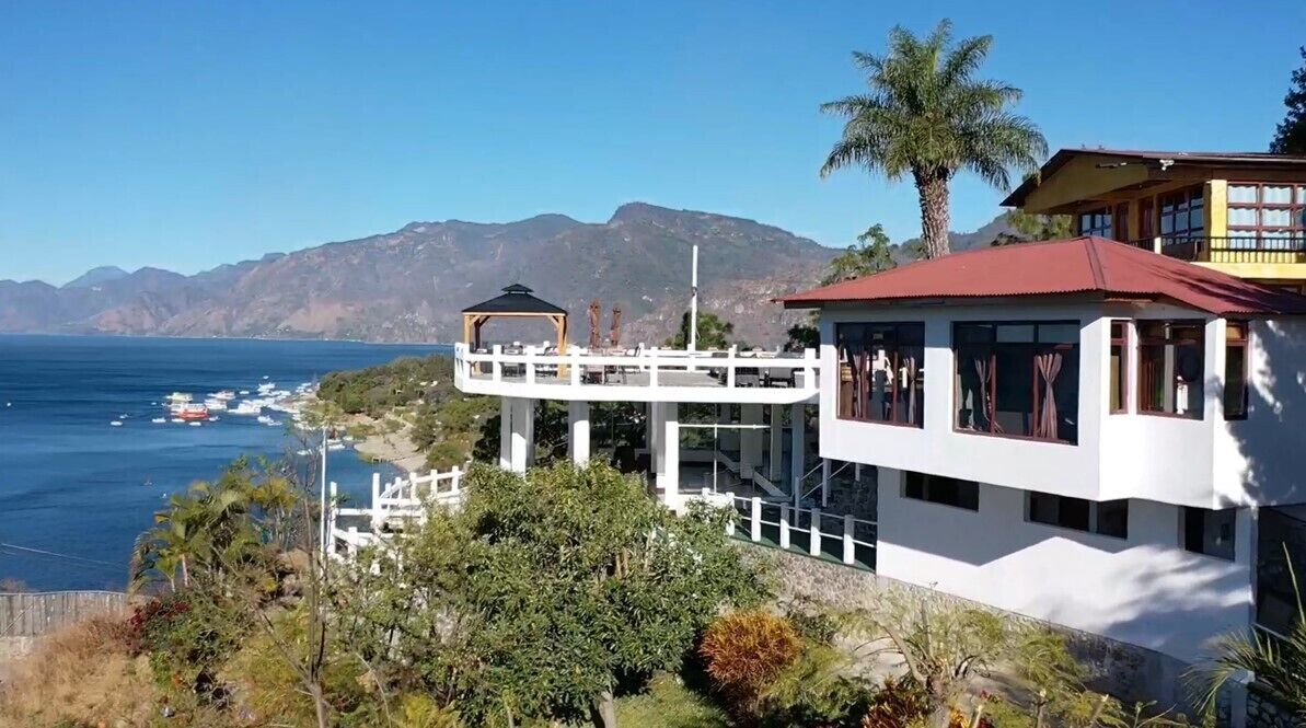 Una propiedad costera con un edificio blanco, una terraza de madera y vistas al océano y las montañas.