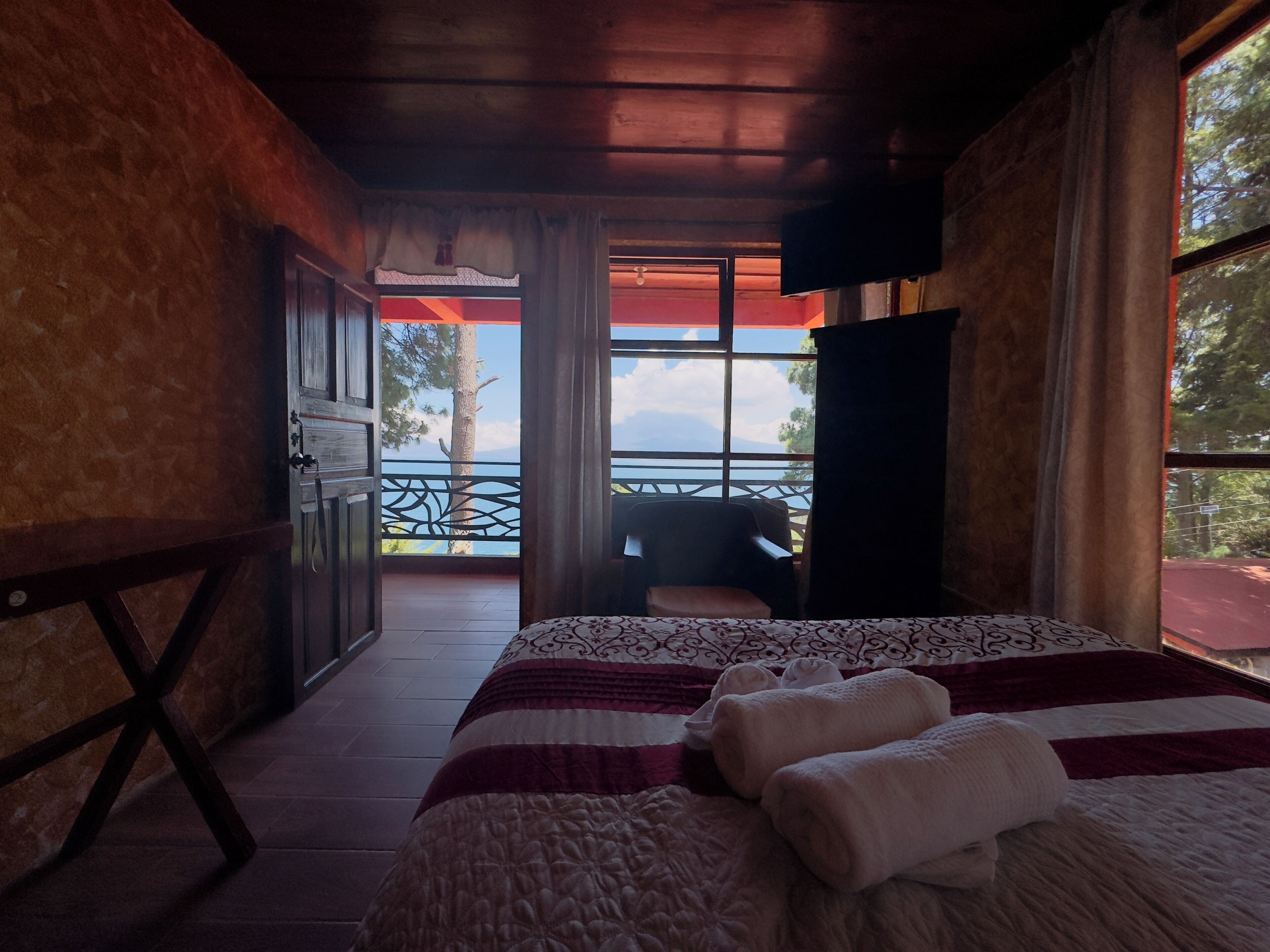 Un dormitorio con cama, una silla, televisor y balcón con vistas.