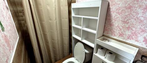 Un baño pequeño con cortina de ducha, inodoro, repisa con artículos de aseo y lavabo.