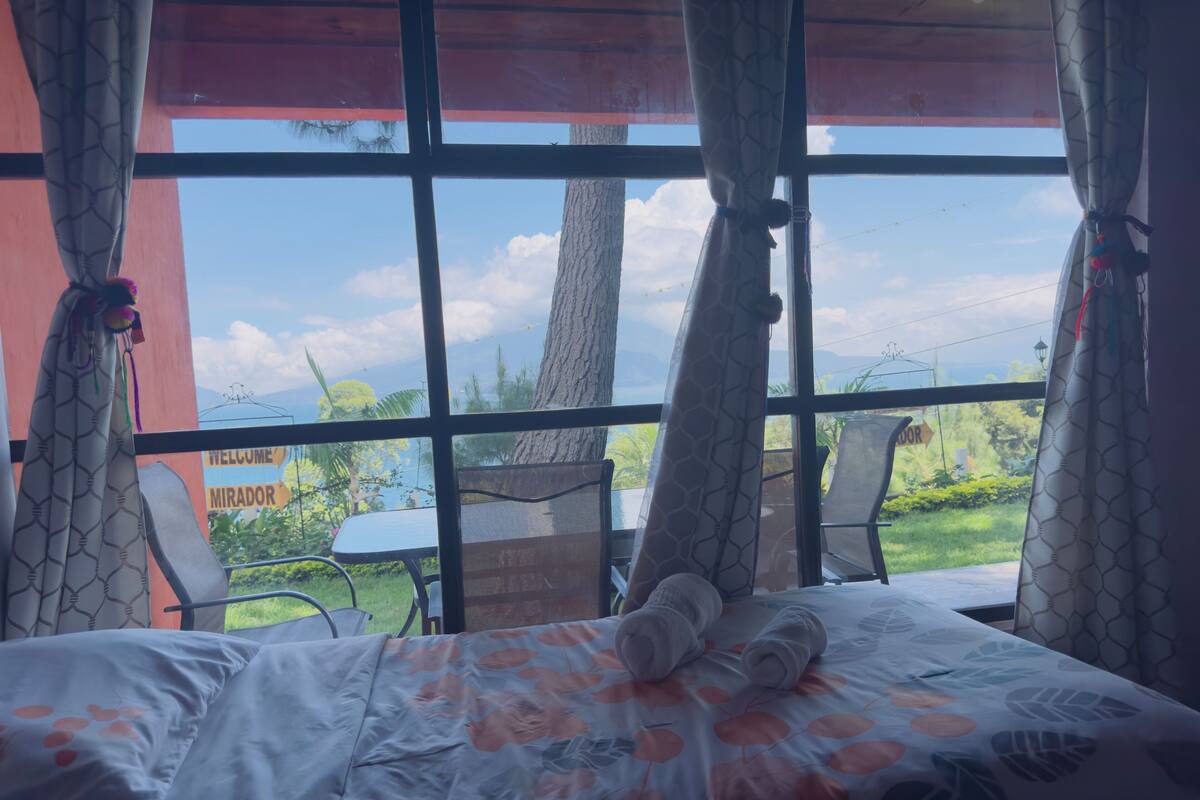 A room with a bed, a view of the outdoors, and a sign with 'WELCOME' and 'MIRADOR' visible.