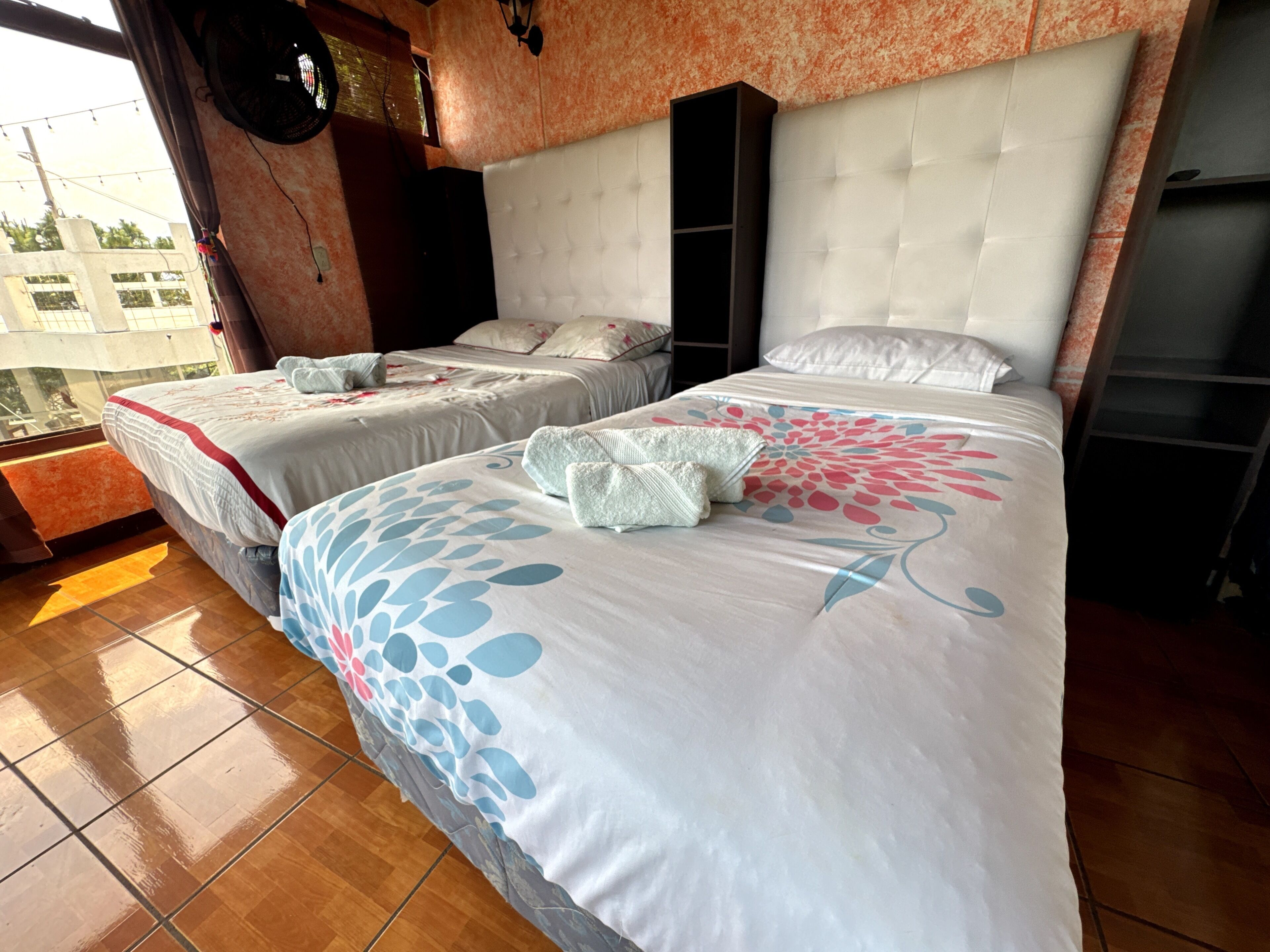 Habitación de hotel con dos camas, un ventanal grande y vistas a edificios.