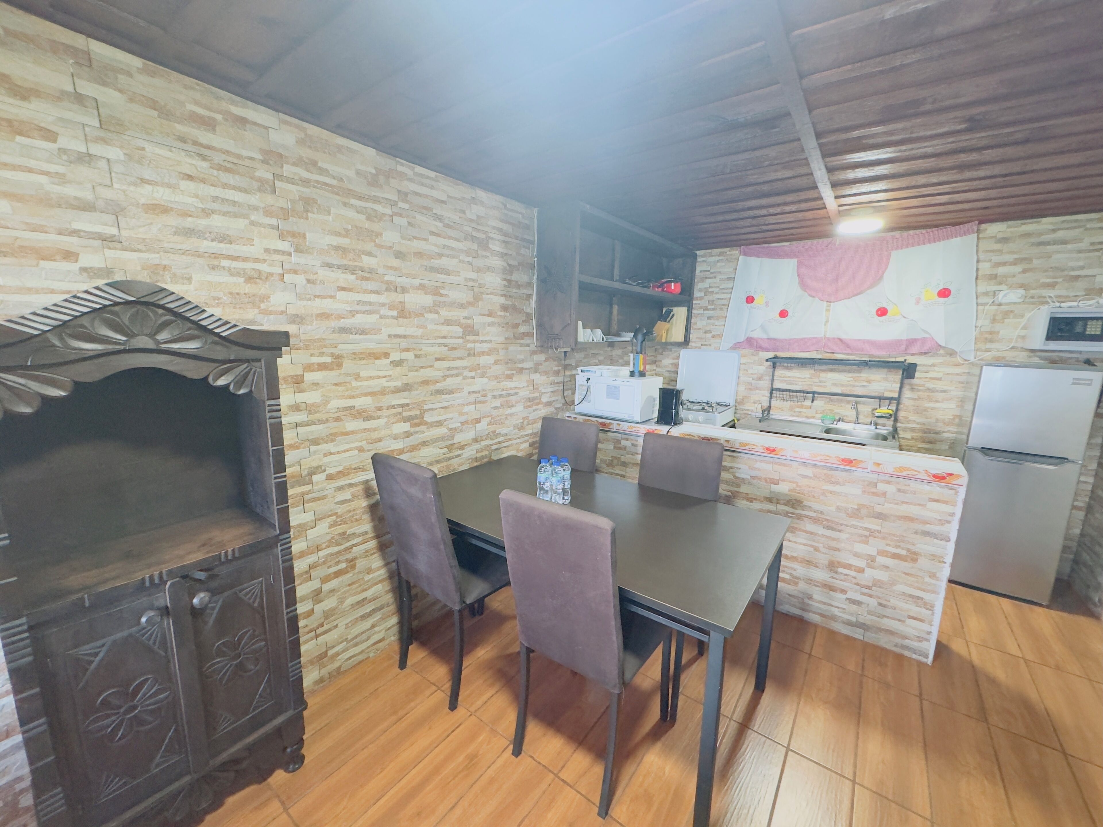 Una cocina con pared de piedra, un mueble de madera, una mesa con sillas, un microondas, un refrigerador y una estufa a gas.