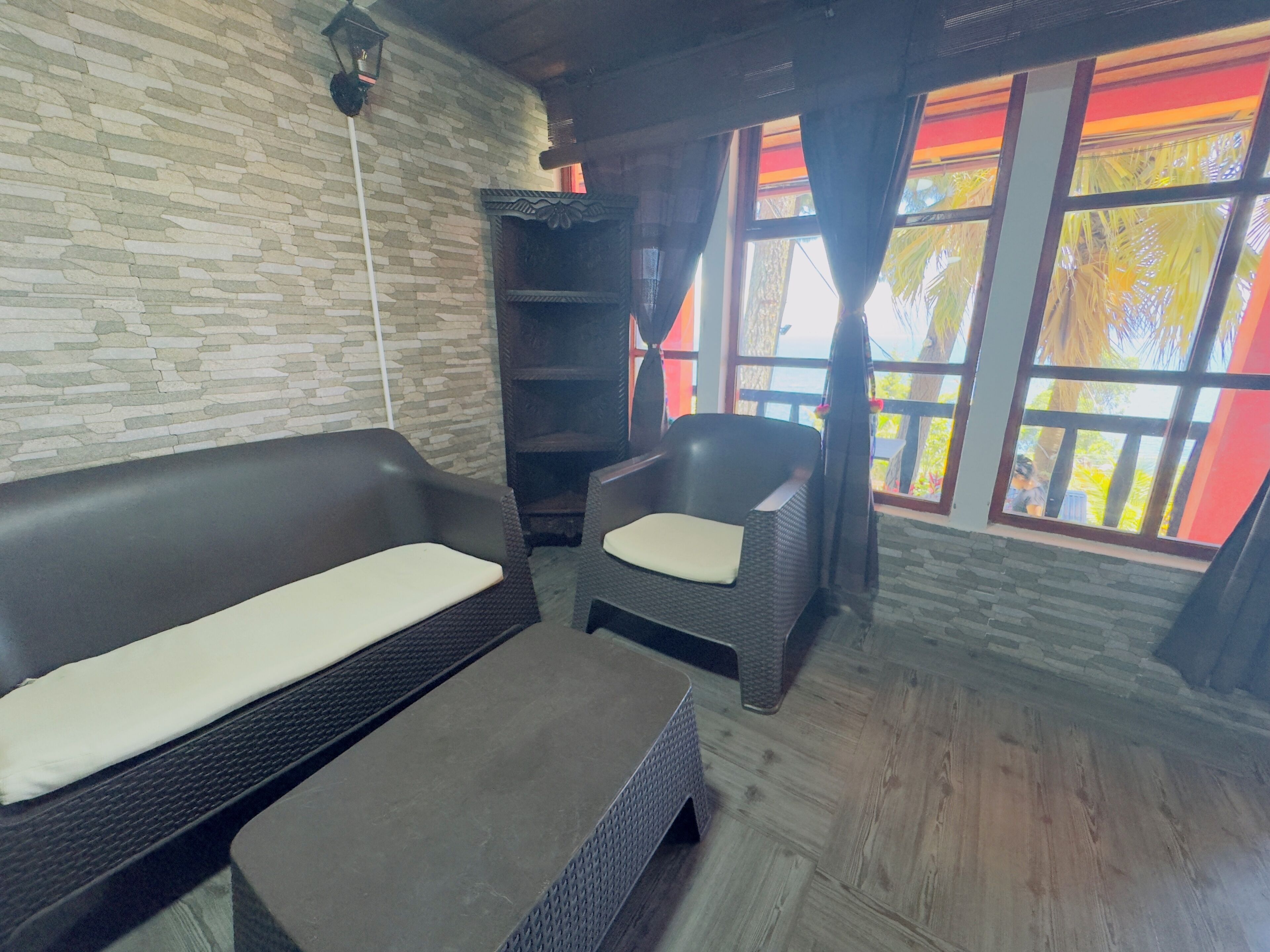 A room with a stone wall, a sofa, a chair, and a window with curtains.