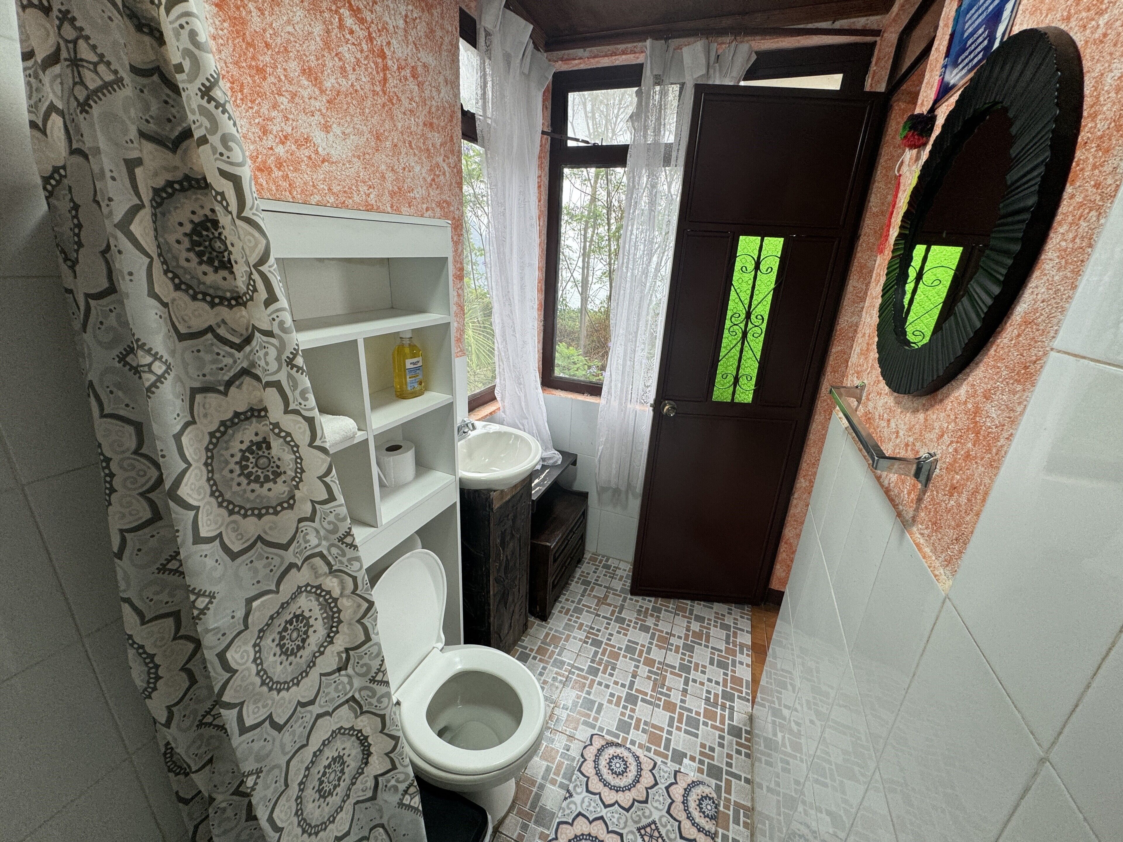 A bathroom with a toilet, sink, patterned floor, and a door with a green window.