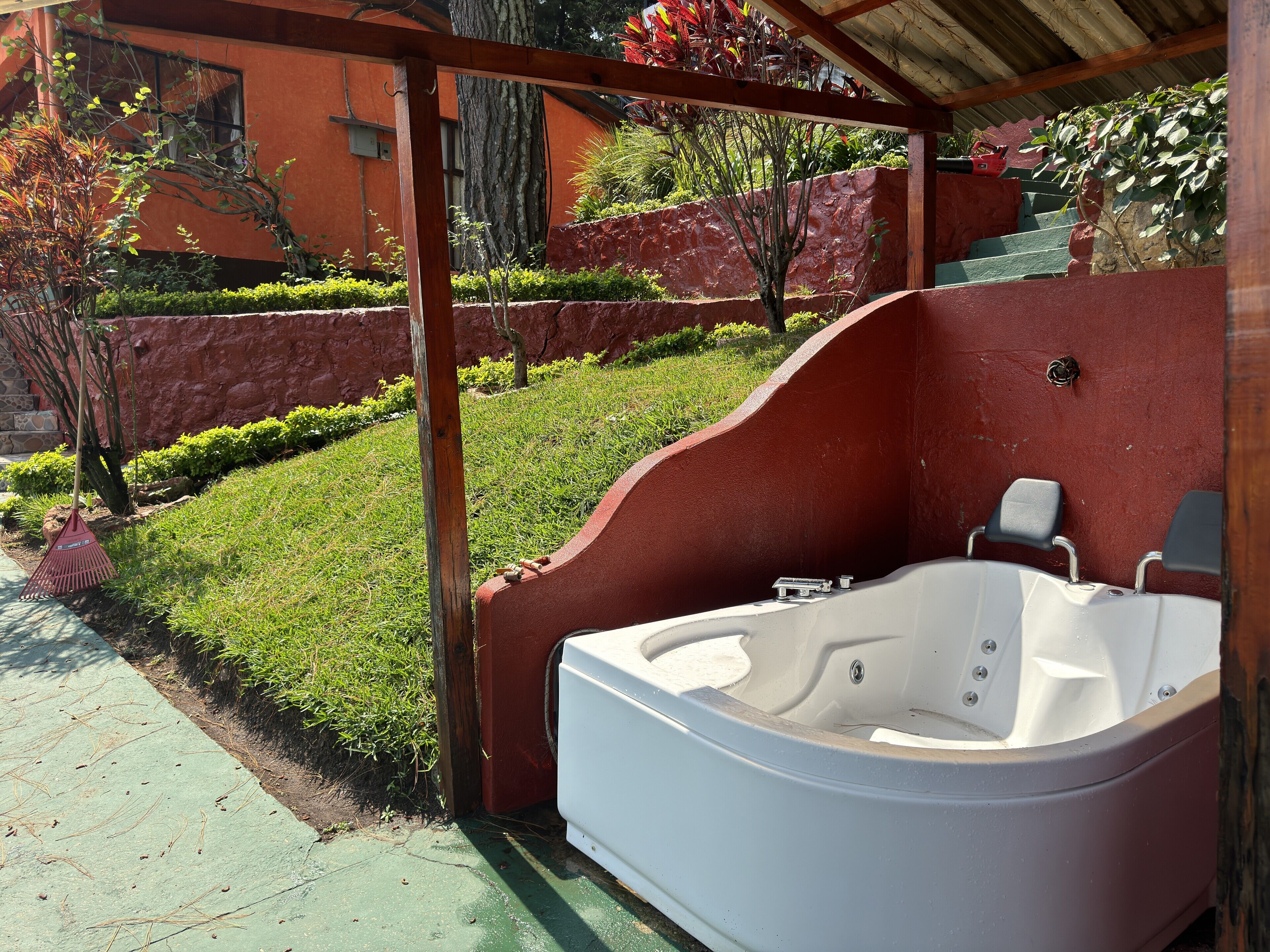 Un jacuzzi en un espacio exterior cubierto con una pared de piedra y vegetación de fondo.