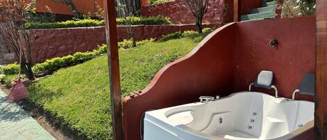 A hot tub in a covered outdoor area with a stone wall and greenery in the background.