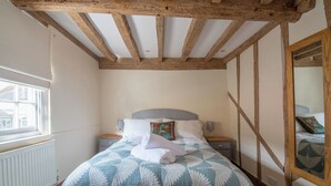 A bedroom with a bed, wooden beams, a window, and a nightstand. - Tegfan – Fairytale Cottage on Dedham High Street (Colchester)