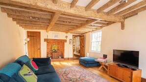 A living room with a blue sofa, wooden beams, a television, and a fireplace. - Tegfan – Fairytale Cottage on Dedham High Street (Colchester)