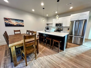 A modern kitchen with a central island, wooden dining table, and chairs. - Luxury Driggs Retreat • Hot Tub • Kids’ Cove • Walk to Town • Near Grand Targhee (Driggs)
