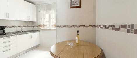 A modern kitchen with white cabinets, a round wooden table, and a window with curtains.