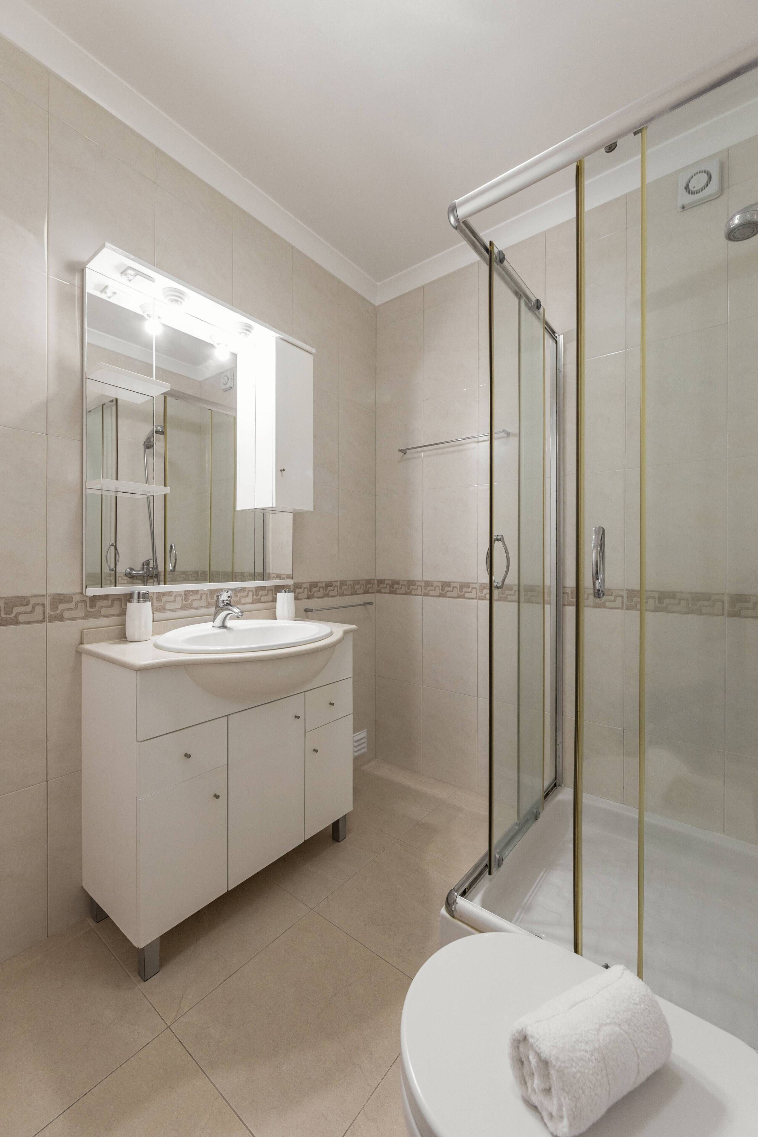 Une salle de bain moderne avec une douche à parois de verre, un lavabo blanc et un grand miroir.