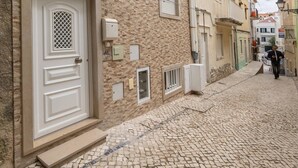 A cobblestone street with buildings featuring traditional architecture, including a prominent white door and a balcony.