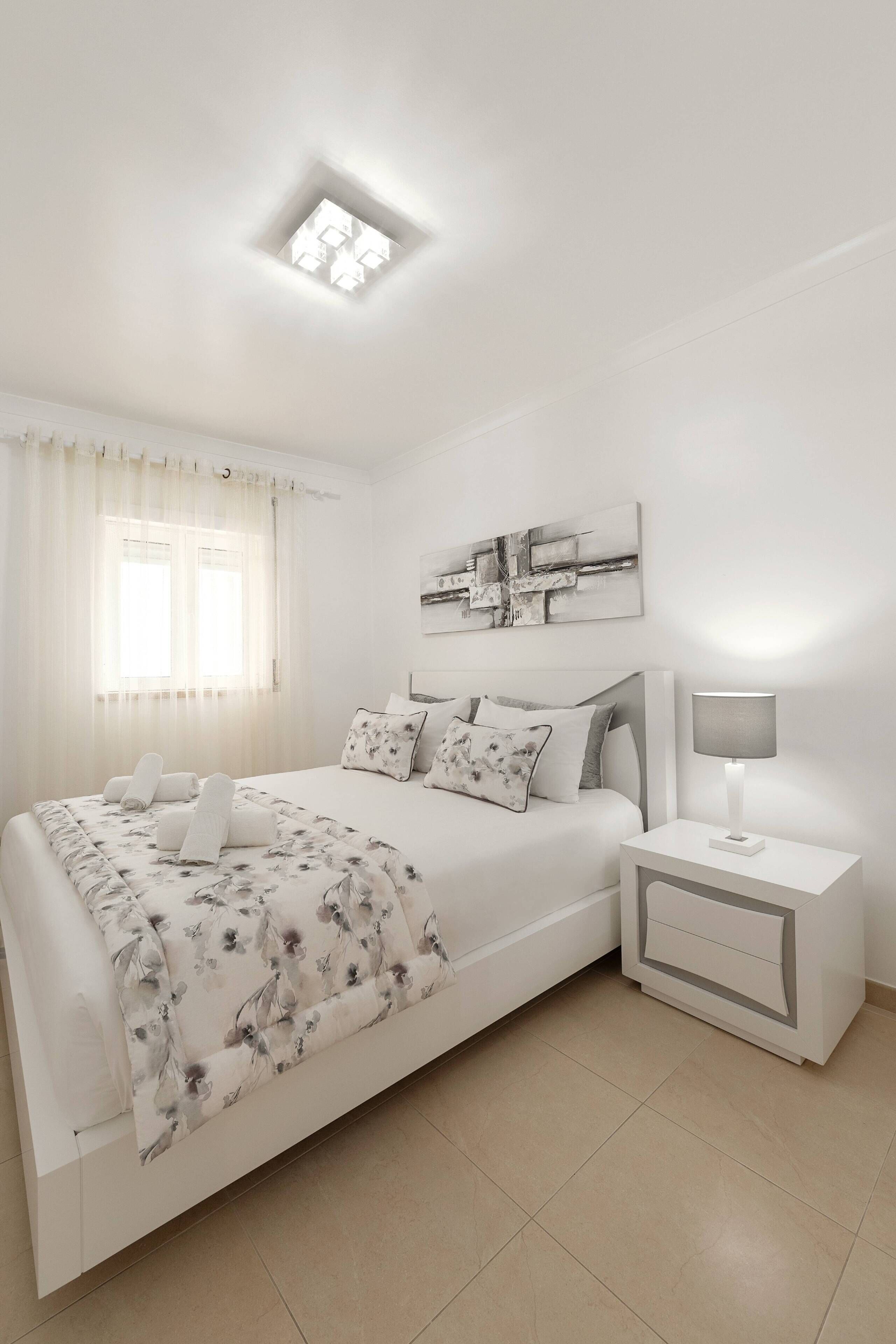 A modern bedroom with a bed, bedside table, and a ceiling light.