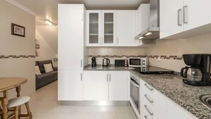 A modern kitchen with white cabinetry, a granite countertop, and a dining area with a wooden table and bar stools.