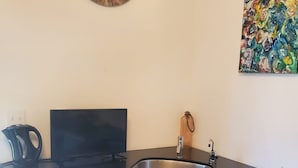 A compact kitchen with a black countertop, white cabinets, a sink, and a painting on the wall.