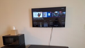 A television mounted on a wall displaying a streaming service interface with various channels and shows. - Leisure Lodge Motel (Grants)