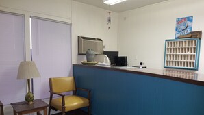 A reception area with a blue counter, a yellow chair, a lamp, a vase, and a security camera. - Leisure Lodge Motel (Grants)