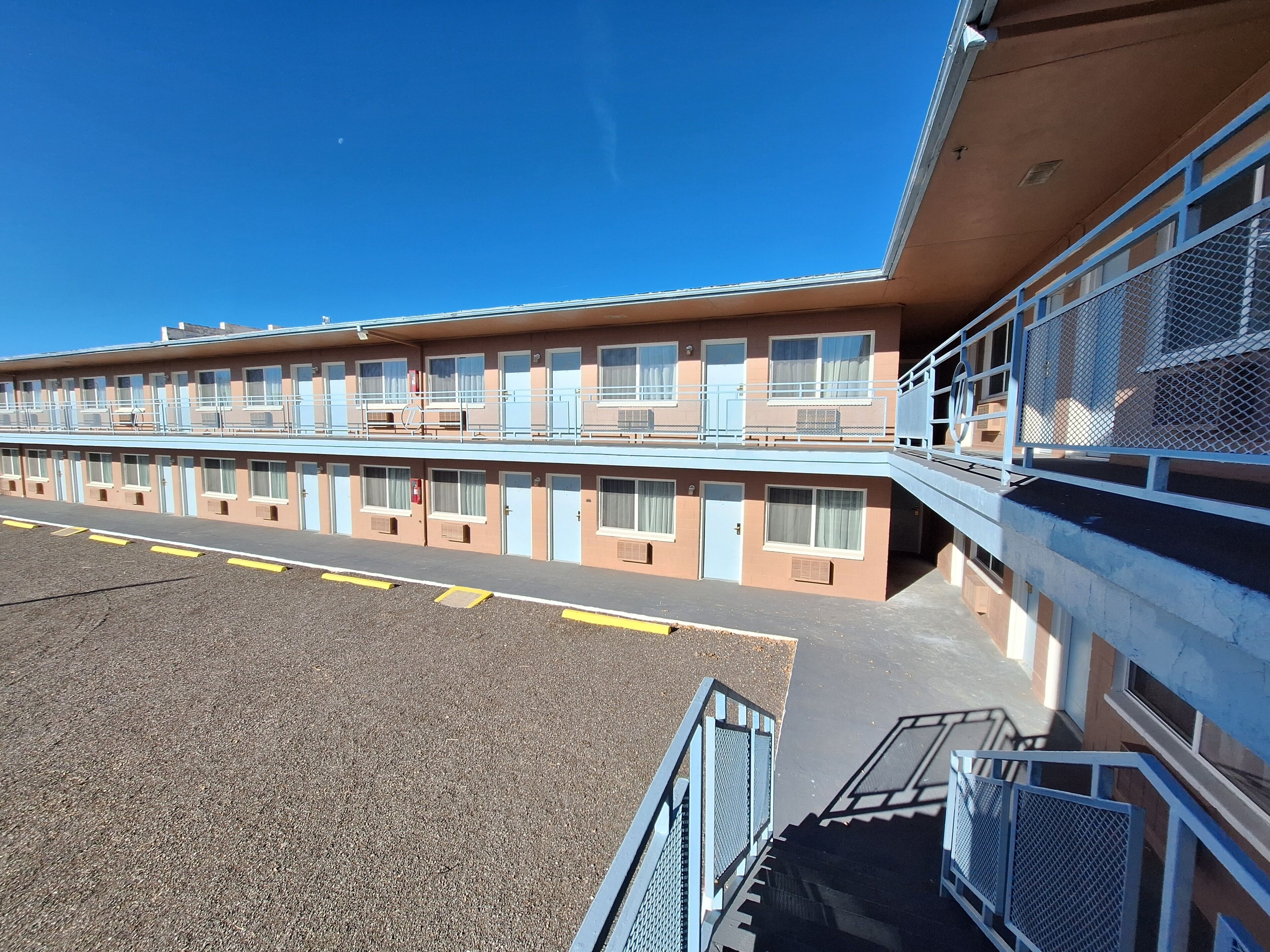 Un motel con varias habitaciones, una zona de estacionamiento techada y una escalera que conduce a un nivel superior.
