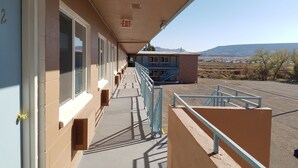 A motel corridor with a covered walkway, a blue building in the background, and a view of a desert landscape. - Leisure Lodge Motel (Grants)
