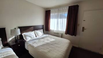 Habitación de hotel con cama, mesita de noche, lámpara, ventana con cortinas y puerta.