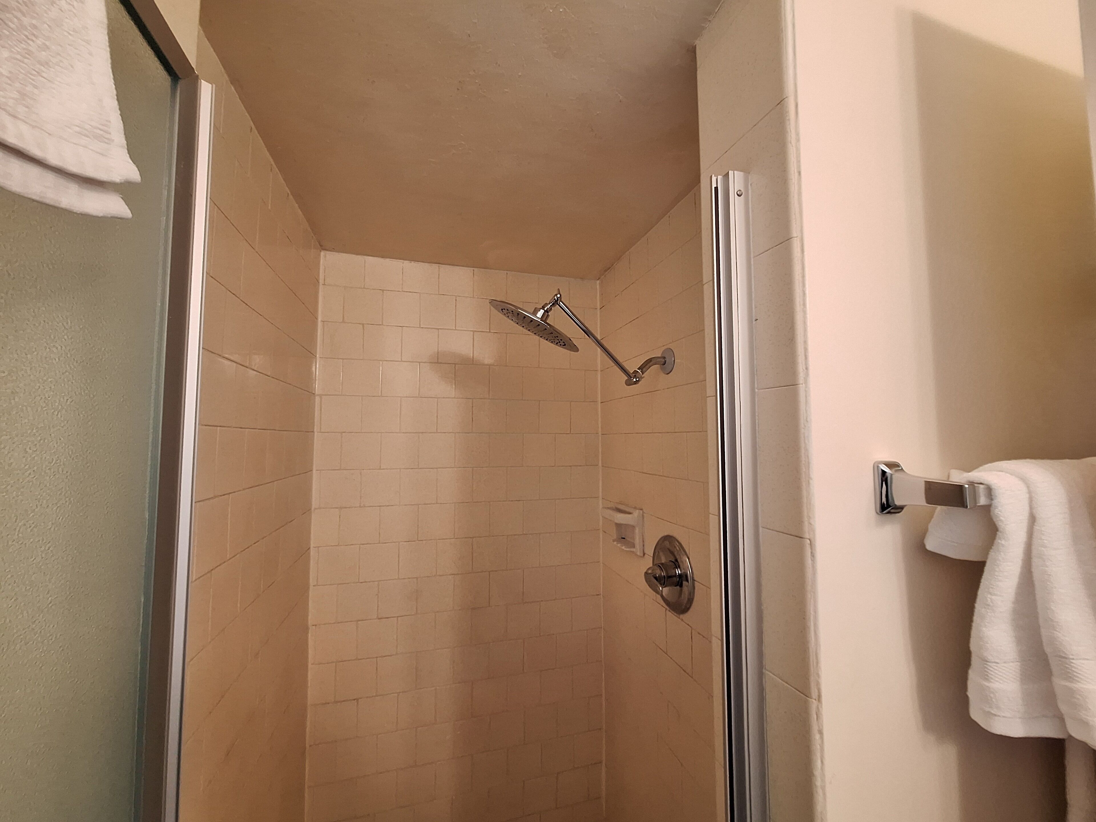 Una ducha con puerta de cristal, paredes de azulejos color beige y un toallero en la pared.
