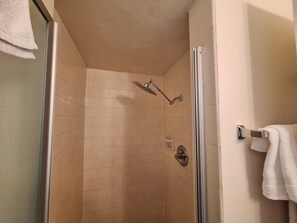 Eine Dusche mit Glastür, beige geflieste Wände und einem Handtuchhalter an der Wand.