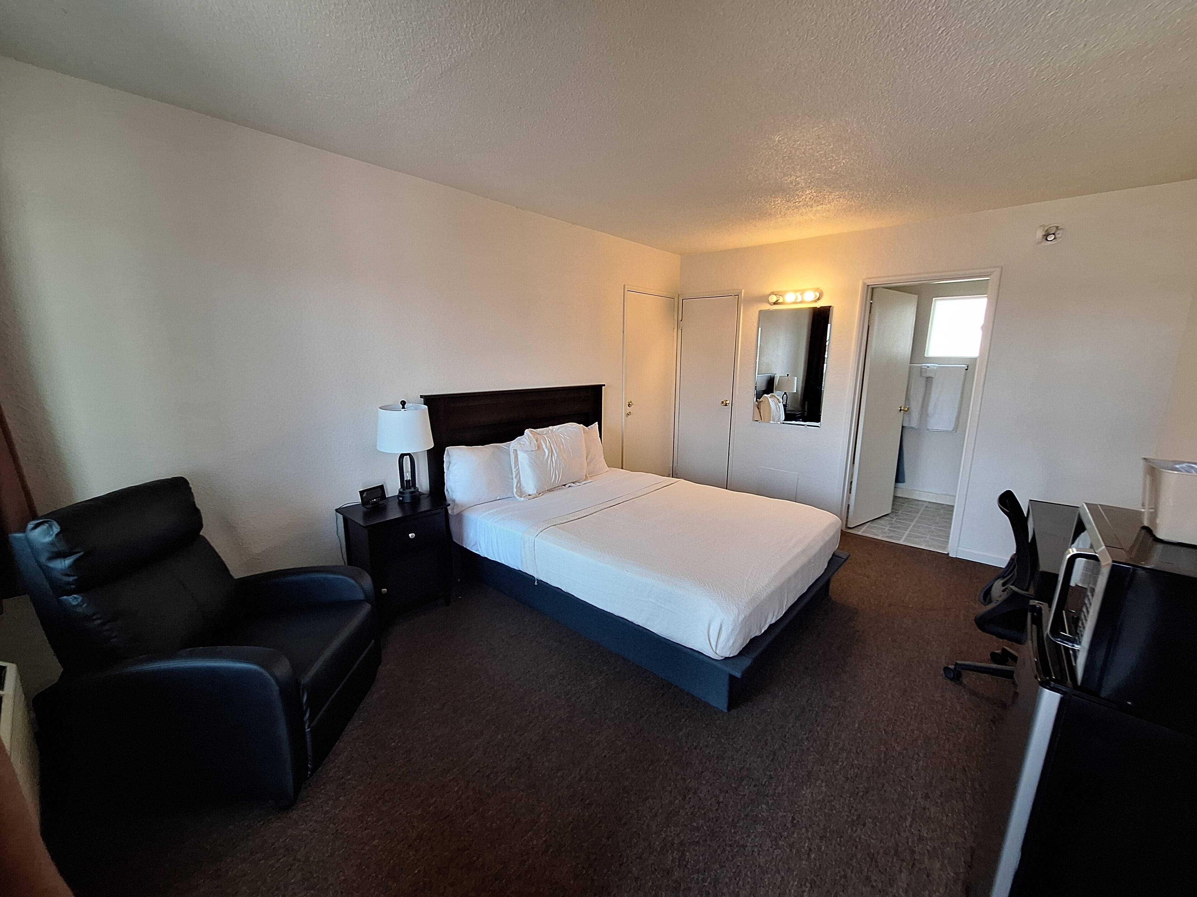 A hotel room with a bed, a chair, a desk, and a wardrobe.
