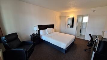 A hotel room with a bed, a chair, a desk, and a wardrobe.