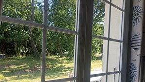 A view through a window with a grid pattern, revealing a grassy outdoor area with trees and a white table and chairs. - House for 10 people in Bois du Kador – surrounded by nature (Crozon)