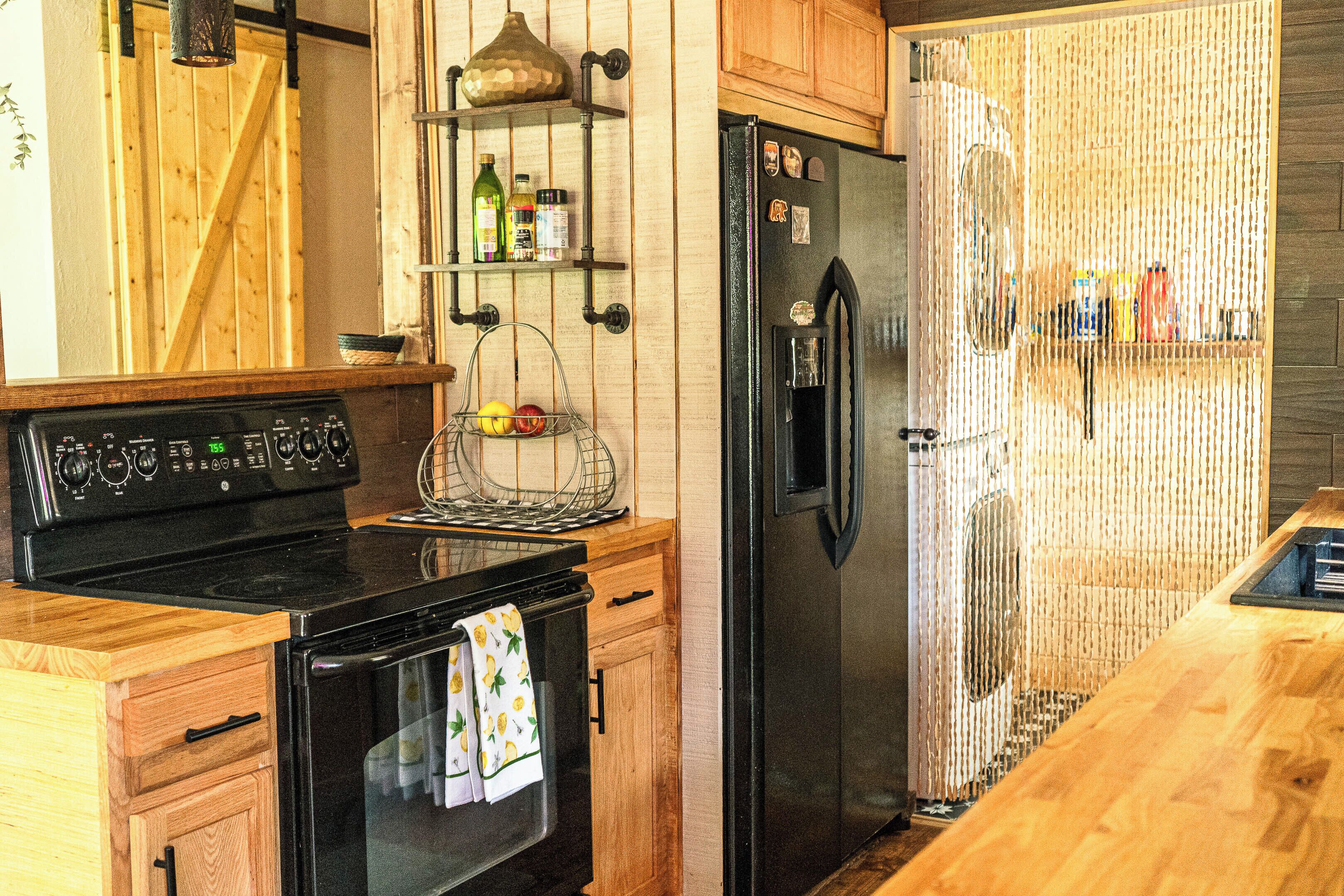 A kitchen with a black stove, oven, and refrigerator, wooden cabinets, and a hanging pot rack.