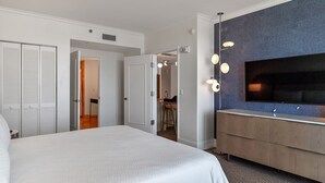 Habitación de hotel con una cama grande, un tocador de madera, un televisor de pantalla plana y un vestidor.