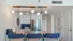 Una cocina moderna con una isla central, electrodomésticos de acero inoxidable y un comedor con sillas azules.
