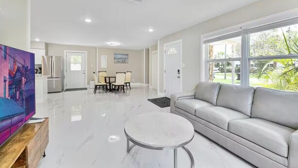 A spacious living room with a sofa, a coffee table, and a dining area with chairs and a table. - 3/2 Cozy and Stylish Poolside Home (St. Petersburg)