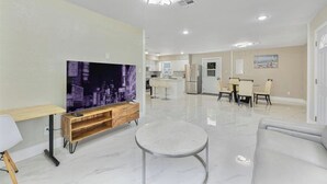 A modern living room with a flat-screen TV, a round coffee table, and a dining area with a kitchen in the background. - 3/2 Cozy and Stylish Poolside Home (St. Petersburg)