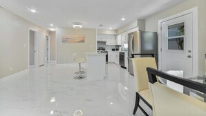 A modern kitchen with white cabinets, a central island, and a dining area with a glass table and chairs. - 3/2 Cozy and Stylish Poolside Home (St. Petersburg)