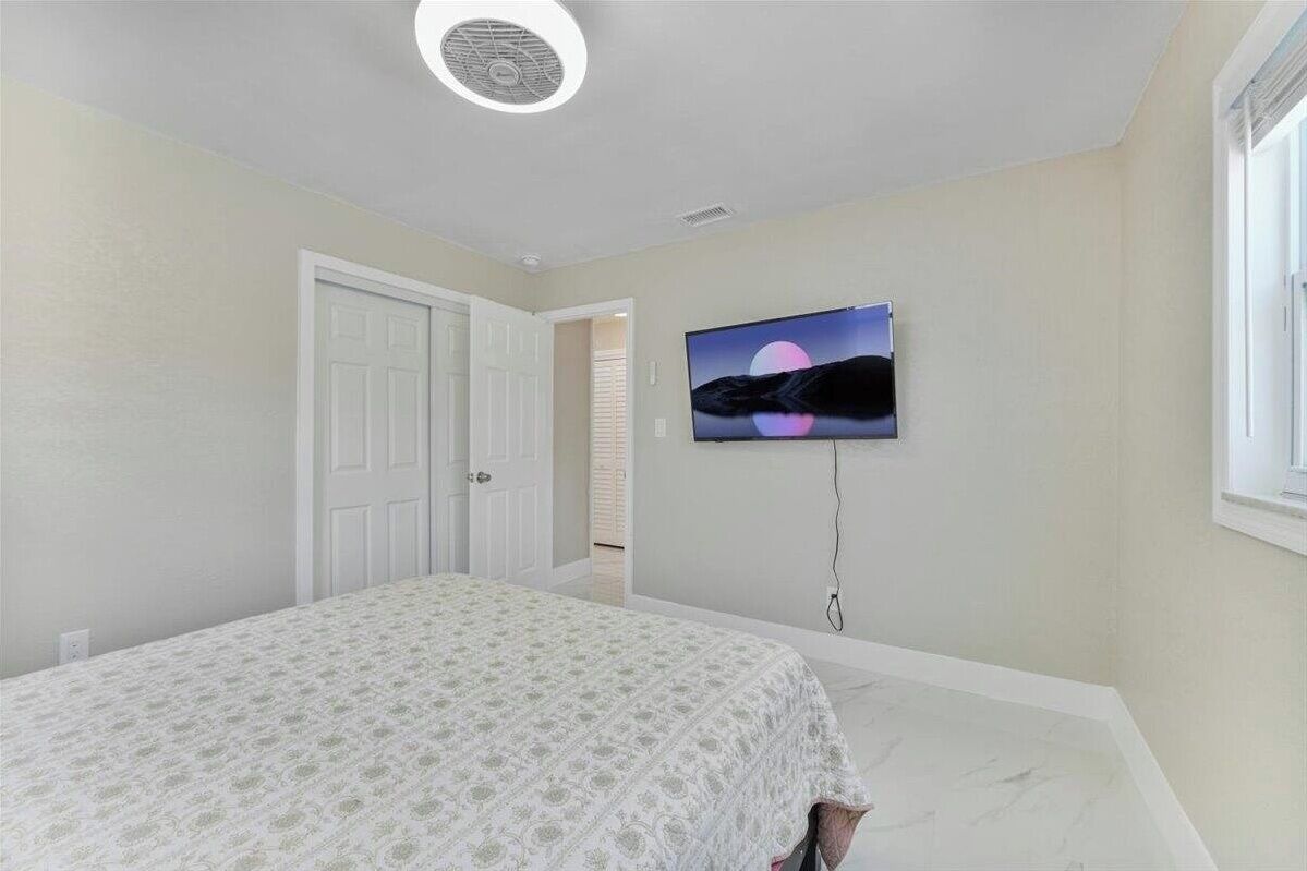 Ein Schlafzimmer mit einem Bett, einem an der Wand montierten Fernseher und einer Tür zu einem anderen Raum.