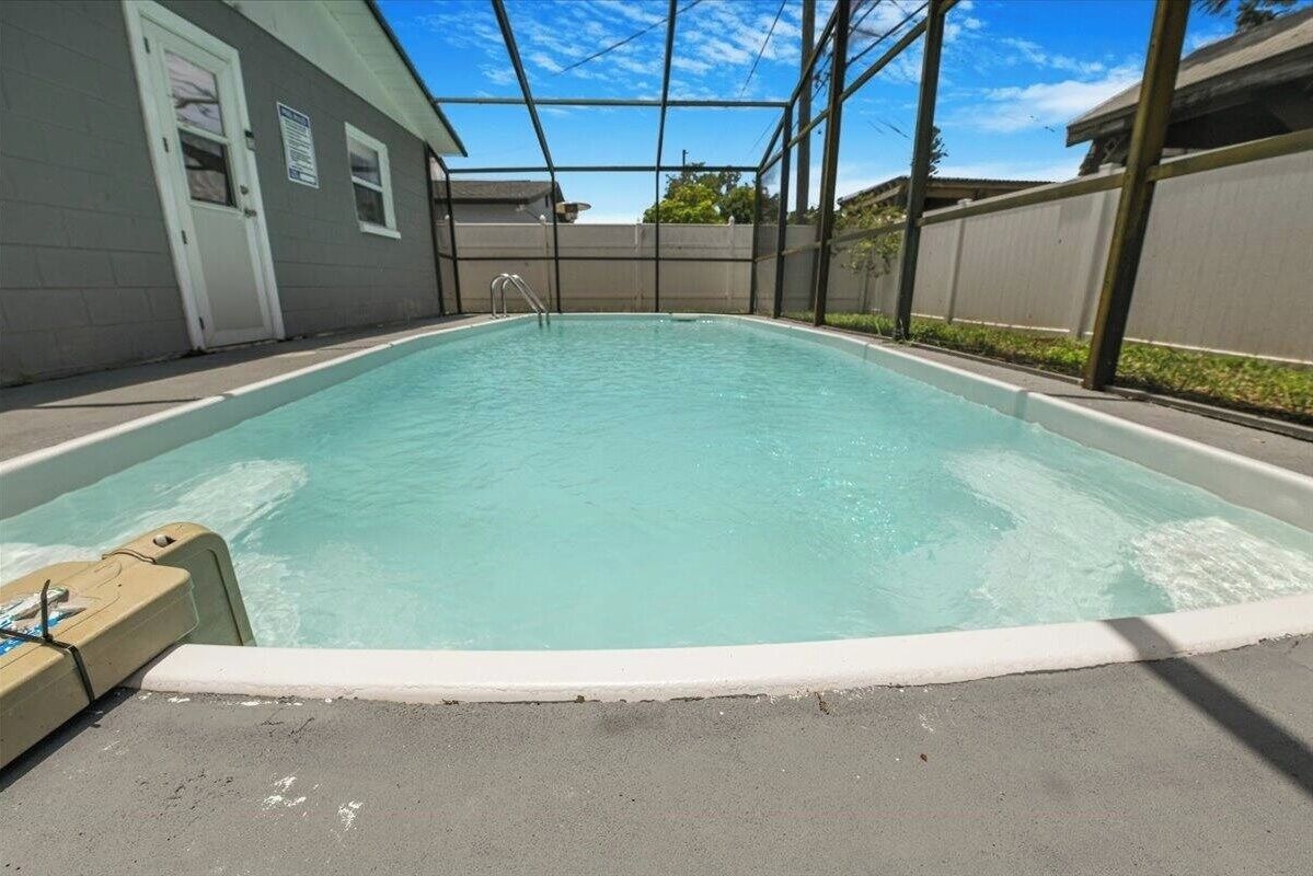 An outdoor swimming pool with a clear blue water, surrounded by a fence and a building.