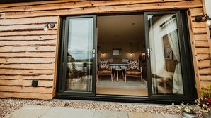 A modern log cabin with a sliding glass door leading to a dining area with a table and chairs.