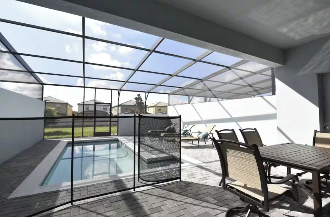 Un patio exterior moderno con cerramiento de vidrio, piscina y mobiliario exterior.