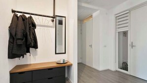 Un pasillo con un banco de madera, un perchero con abrigos, un espejo y un armario.