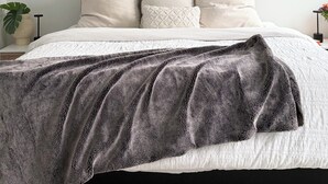 Un lit avec une couverture à motifs gris et blancs, une tête de lit grise et deux oreillers blancs.