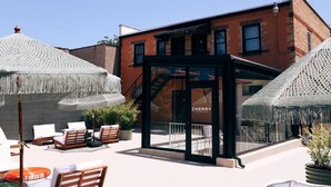 A modern outdoor seating area with white chairs and tables, a glass entrance to a building labeled "CHERRY," and a brick building in the background.